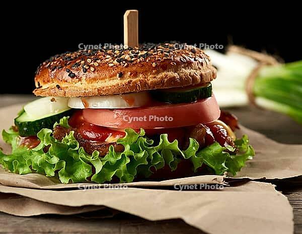 Cheeseburger with minced meat, green lettuce and ketchup on a wooden brown kitchen board, close up [IBR125331179]