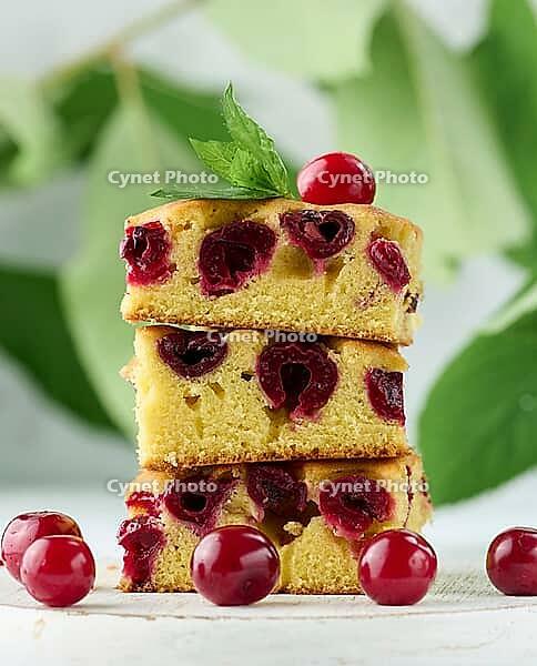 Baked pieces of sponge cake with red ripe cherries on a white wooden board [IBR125331185]