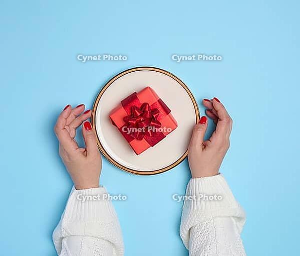 Two female hands holding a plate with a gift on a blue background, top view [IBR125344243]