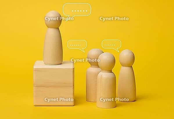 Wooden figures on a yellow background symbolize communication and leadership, one figure stands on a pedestal, representing a speaker conducting a dialogue with a team discussing ideas and solutions [IBR125344249]