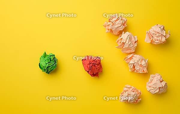 Crumpled sheets of colored paper on a yellow background. Solution concept, brainstorming, opposition and confrontation, mediator in resolving the issue [IBR125344254]