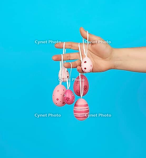 Female hand holds easter colored pink eggs on a rope, blue background [IBR125344295]