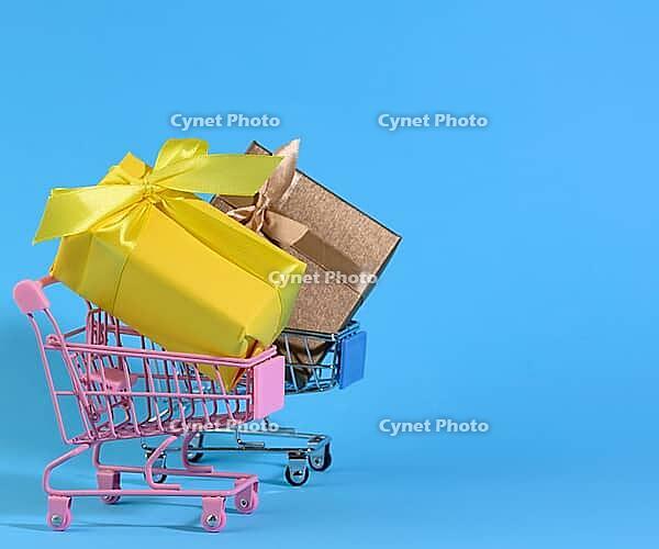 Yellow gift box with a silk bow in a miniature metal trolley on a light blue background. Party Backdrop, Surprise, Seasonal Sale [IBR125344302]
