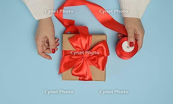 Two female hands holding gift boxes tied with a red ribbon on a blue background. Top view [IBR125344304]