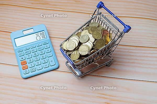Coins filling a miniature shopping cart with a calculator on a wooden table, representing financial planning and budgeting [IBR125344313]