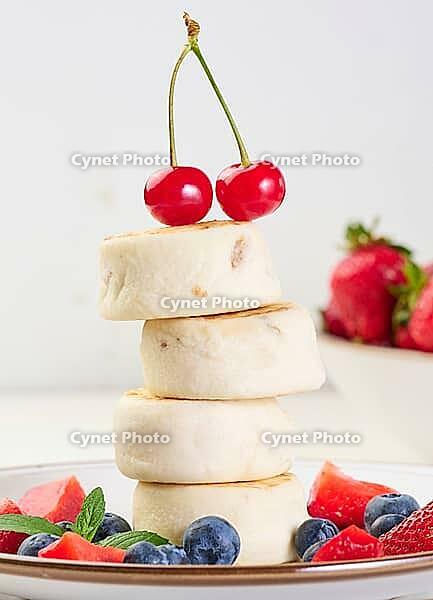 A stack of four cheesecakes on a plate with berries, blueberries, strawberries and cherries. Background white [IBR125344332]