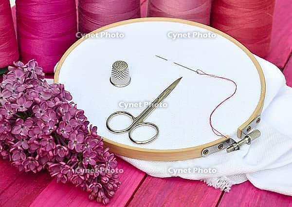 White cloth in wooden embroidered embroidery frame, behind a row of thread reels in red [IBR125363545]