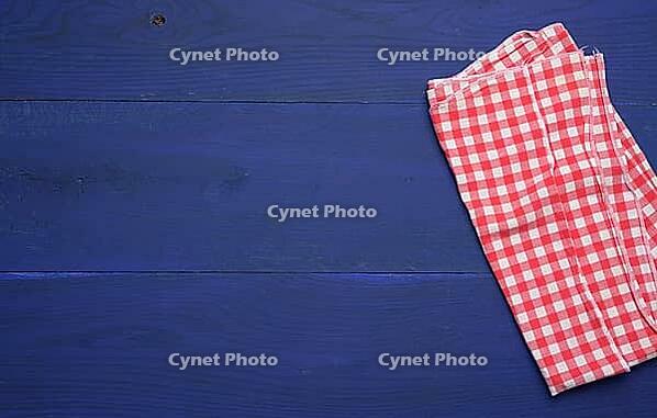 Folded red and white cotton kitchen napkin on a wooden blue background, top view, copy space [IBR125363547]