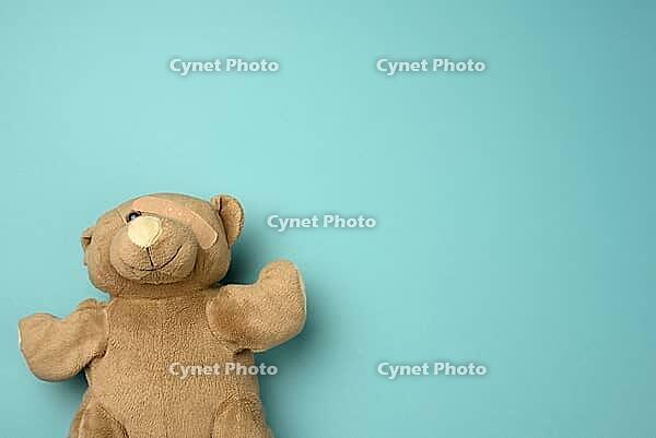 Old teddy bear with a band-aid on the eye lies on a blue background, top view, copy space [IBR125363568]