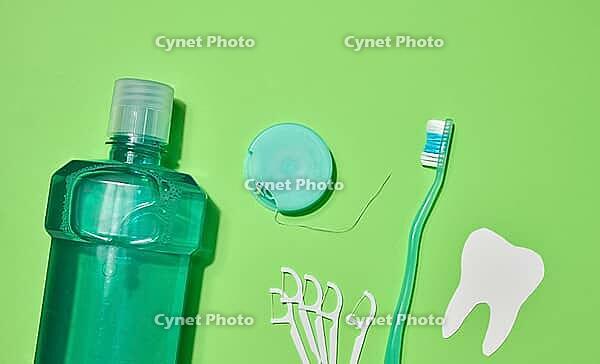 Green toothbrush, mouthwash bottle, dental floss in case, plastic floss holders on green background. Top view [IBR125363573]