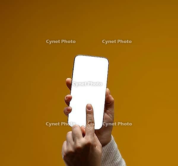 Close-up of female hands holding modern smartphone with blank white screen. Yellow background. Mock up [IBR125363614]