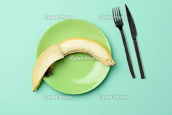 Round green ceramic plate with a whole banana and knife and fork on a green background, diet, top view [IBR125382567]