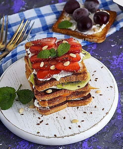 A pile of French toast with cottage cheese, strawberries, kiwi and blueberries on a round white wooden board, top view [IBR125382594]