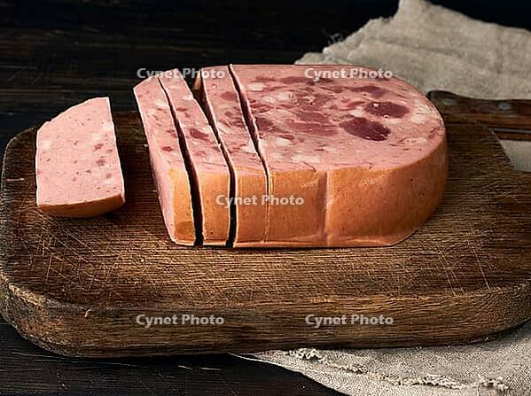 Sliced boiled sausage with slices of whole meat on a brown wooden cutting board, close up [IBR125382612]