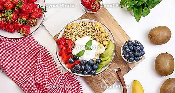 Granola with strawberries, kiwi, banana and blueberries in a round plate on a white table. Healthy and tasty food, top view [IBR125382628]