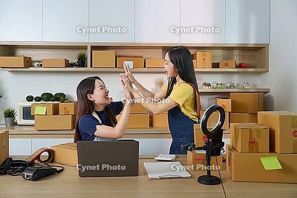 Young woman show joy and teamwork as they complete e-commerce tasks in a lively office environment [IBR125382655]