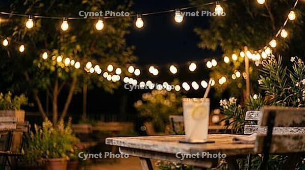 String of Warm Bulbs over a Summer Terrace at Night with Blurred Lemonade Glass, Festive Glow Bokeh Background with Copy Space, AI generated [IBR125395918]