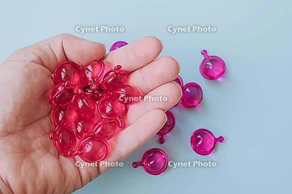 Pink hair vitamin capsules in a woman's hand on a light blue background. [IBR125405006]
