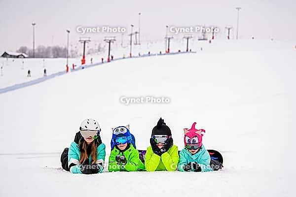 Group of children and teenagers lie in the snow at a ski resort. Ski lifts and skiers are visible in the background. The atmosphere is cheerful and carefree, emphasizing the joy of winter recreation [IBR125405008]