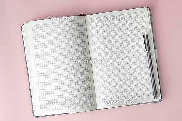 Open notebook with squared paper and pen on pink background, symbolizing creativity, planning, education, productivity, and clean workspace for notes or design projects, copyspace [IBR125405068]