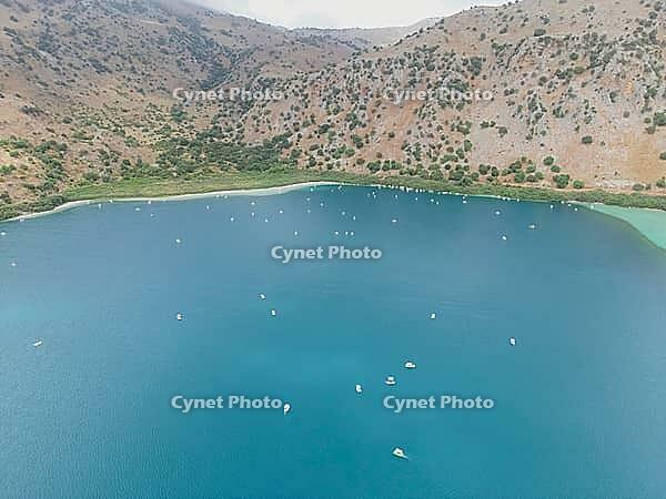Kournas Lake at the foot of the mountains during peak tourist season, with many visitors enjoying pedal boats in clear sunny weather on Crete island [IBR125405083]