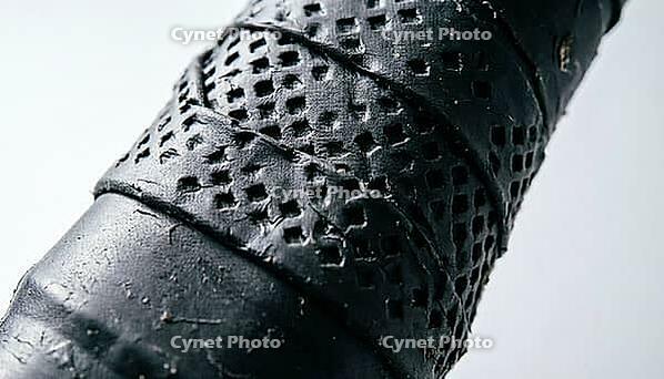 Extreme close-up of black perforated tennis racket grip tape texture with spiral wrap and overlapping seam, raking studio light, full frame texture, sports equipment concept, AI generated [IBR125407383]
