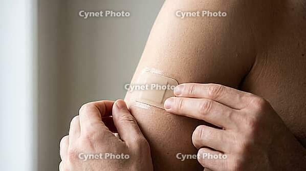 Adult hands applying a small plain beige nicotine patch to the opposite upper arm, fingers smoothing the edge, soft natural daylight, no face visible, smoking cessation health concept, AI generated [IBR125407395]