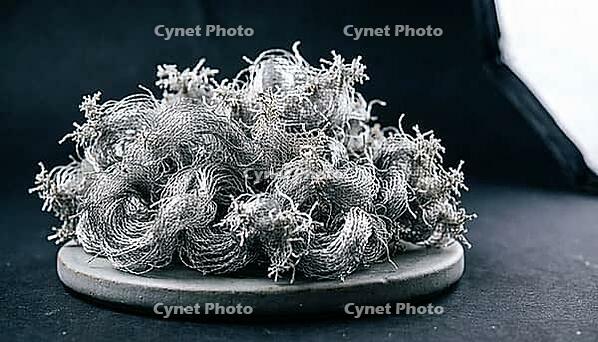 Dense diffuse cluster of fine metallic lithium dendrite filaments in a fluffy mossy formation on dark ceramic substrate, charcoal background, industrial lighting, battery failure science, AI generated [IBR125407422]