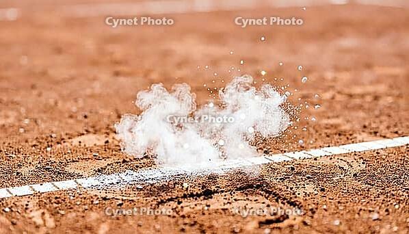 Fine white chalk dust suspended mid-air above a reddish-orange clay tennis court's boundary line, freshly disturbed mark below, bright daylight, decisive line call sports concept, AI generated [IBR125407427]