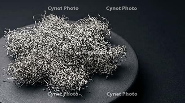 Dense diffuse cluster of fine metallic lithium dendrite filaments in a fluffy mossy formation on dark ceramic substrate, charcoal background, industrial lighting, battery failure science, AI generated [IBR125407430]