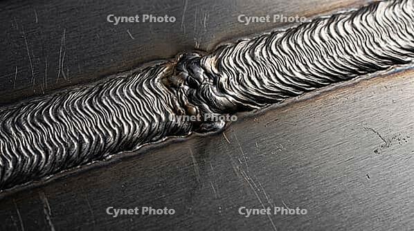 Close-up of two overlapping solidified metal weld tracks with fine ripple texture and a subtle remelted seam, full frame texture, industrial macro photography, additive manufacturing, AI generated [IBR125407449]