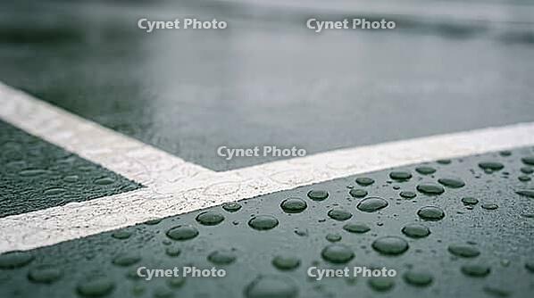 Scattered raindrops on a smooth dark green hard tennis court surface beside a faint white line, soft overcast daylight, no players visible, rain delay sports concept, AI generated [IBR125407462]