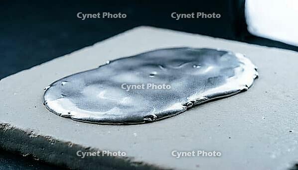 Smooth continuous metallic lithium deposition layer spreading laterally across a flat pale grey ceramic substrate, charcoal background, industrial lighting, high temperature battery science, AI generated [IBR125407470]