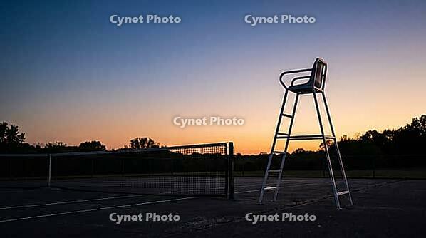 Empty white umpire chair silhouetted against a gradient dusk sky beside an unmarked tennis court, warm horizon light fading to deep blue, quiet reflective mood, sports atmosphere concept, AI generated [IBR125407472]