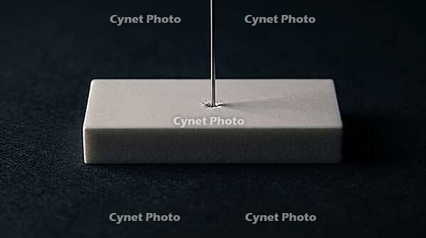 Thin silver-grey metallic lithium dendrite filament piercing through a fracture point in a solid crystalline ceramic block, charcoal background, studio lighting, battery failure science, AI generated [IBR125407476]