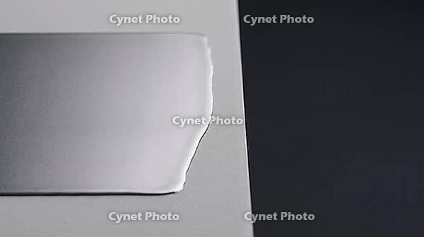 Smooth continuous metallic lithium deposition layer spreading laterally across a flat pale grey ceramic substrate, charcoal background, industrial lighting, high temperature battery science, AI generated [IBR125407477]