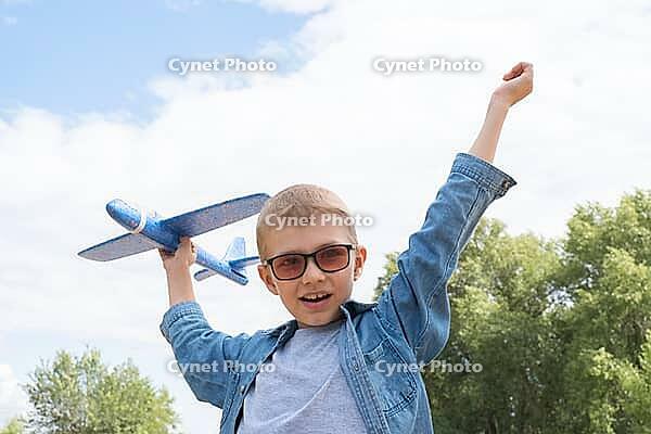 Happy child playing with a toy airplane against a blue sky in an open field [IBR125411099]