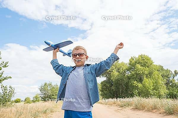 Portrait of a happy child playing with a toy airplane against a blue sky in an open field [IBR125411104]