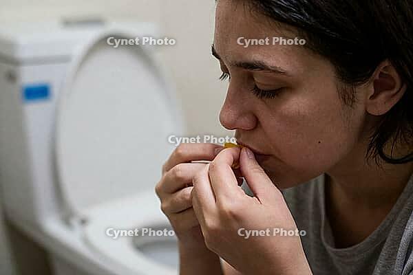 Young woman dealing with nausea, bulimia nervosa, morning sickness, medication intake and psychological distress next to an open ceramic toilet bowl, intimate moment of vulnerability reflecting somatization disorders and gastrointestinal pain, physiologic [IBR125414136]