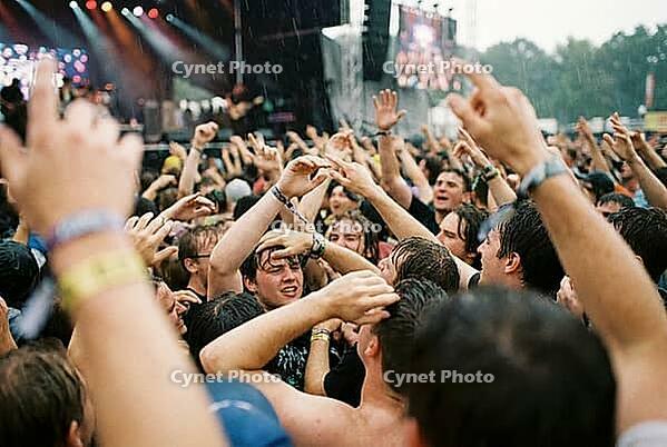 Ecstatic music festival crowd celebrating live open air performance in heavy summer rain, energetic youth culture, collective euphoria and catharsis, drenched concertgoers raising hands in physical communion during rock show, vibrant mosh pit atmosphere r [IBR125414145]