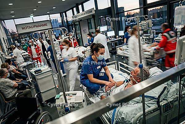 Emergency room healthcare crisis in intensive medical care, dedicated nurse comforts elderly patient on hospital bed during critical triage situation, frantic clinical environment full of paramedics and doctors managing severe overload in clinical hallway [IBR125414146]
