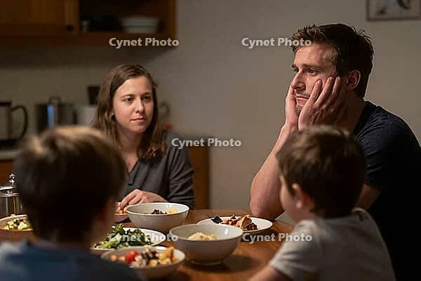 Exhausted parents face emotional burnout at family dinner table, domestic tension and psychological stress challenge young household dynamics, father resting chin in hands reveals mental fatigue and overwhelming parental responsibility, mother observing q [IBR125414169]