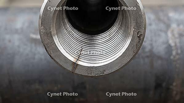 Head-on view of a threaded steel pipe joint opening with a fine crack radiating from the rim, circular thread geometry, industrial macro photography, structural failure investigation, AI generated [IBR125414175]