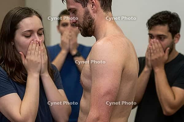 Vulnerable shirtless man experiencing collective shock, social stigma and intense emotional distress surrounded by stunned gasping companions, somatic expression of sudden trauma and exposure, psychological confrontation within an interpersonal group sett [IBR125414187]