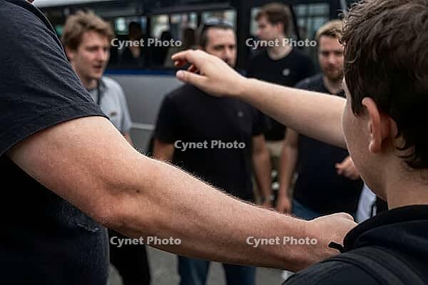 Interpersonal conflict, group dynamics, nonverbal communication in urban spaces, physical gestures, outstretched arms frame tense social interactions among young men gathered near a transit vehicle, intense body language and defensive posture serve as a v [IBR125414193]