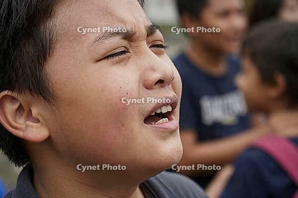 Emotional facial expression of a squinting boy outdoors, intense human reaction, adolescent vulnerability and raw sensory perception, grimacing youth experiencing emotional friction or bright blinding daylight among peers, close up view of authentic affec [IBR125414195]