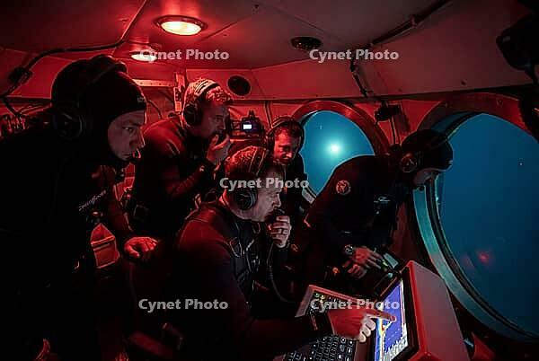 Deep sea underwater exploration crew inside submarine cockpit with sonar navigation monitoring, marine research team in diving suits analyzing bathymetric charts, circular porthole windows revealing dark ocean water illuminated by external submersible spo [IBR125414196]