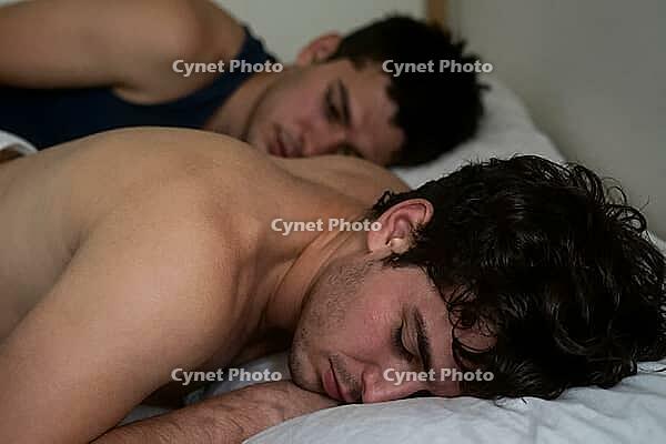 Gay male couple sleeping peacefully in bed, morning intimacy, deep emotional vulnerability, psychological safety in domestic partnership, quiet rest, young shirtless man resting face down beside partner on white linen sheets, non verbal communication of t [IBR125414201]