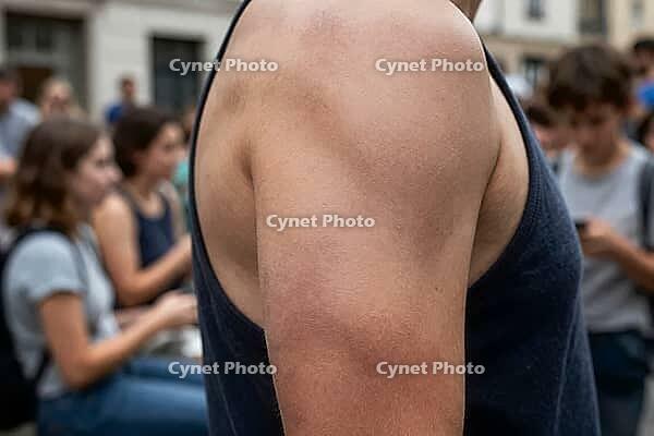 Athletic male shoulder and muscular arm in sleeveless shirt standing in crowded urban street setting during warm summer season, skin texture and anatomical definition highlighting body culture and physical wellness in contrast to digital distraction, blur [IBR125414204]