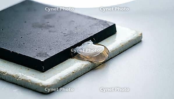 Close-up of translucent amber grey epoxy underfill resin flowing by capillary action beneath a silicon chip edge, ceramic substrate, semiconductor packaging macro photography, AI generated [IBR125421187]